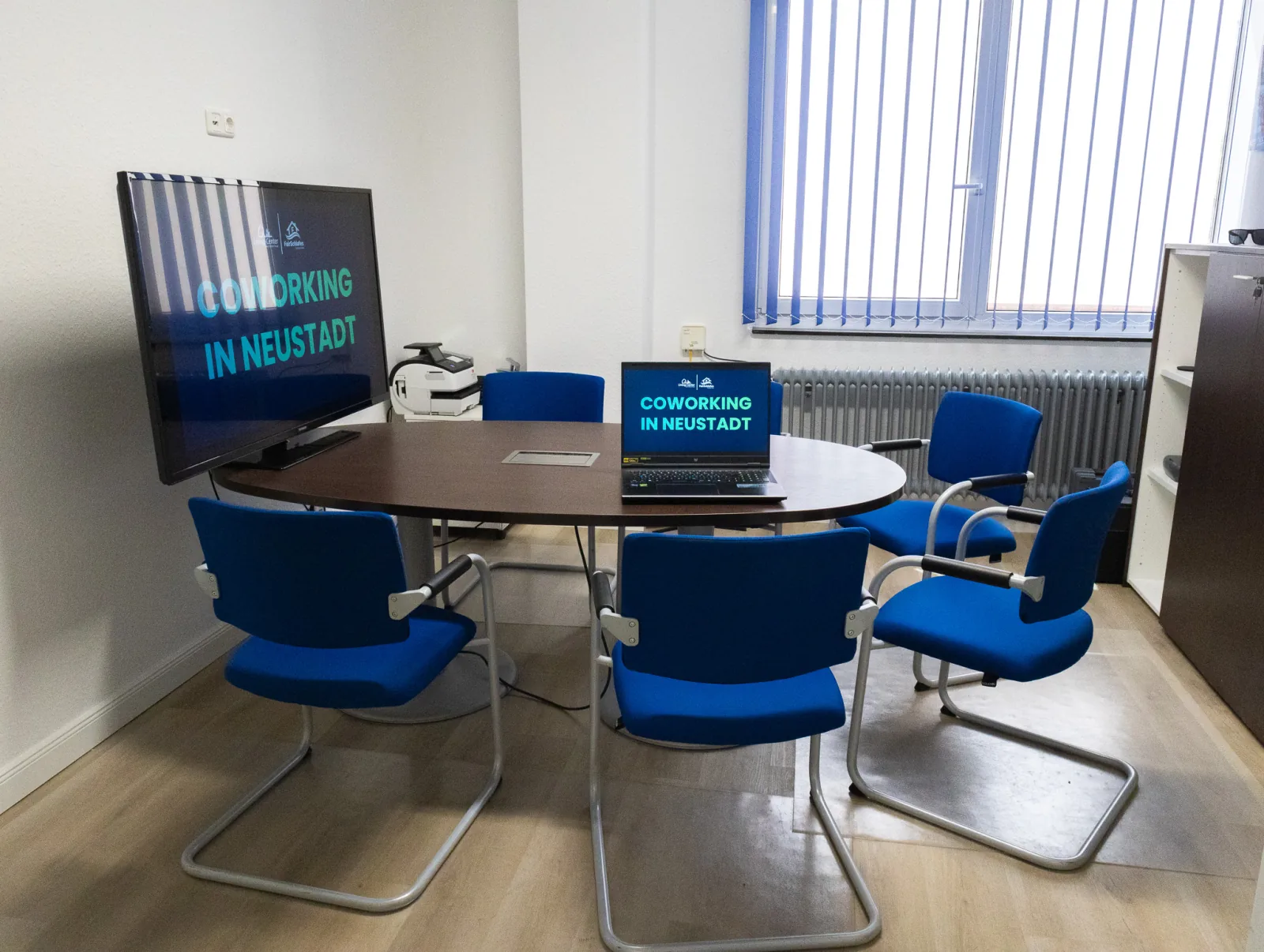 Runder Besprechungstisch mit blauen Stühlen und Fernseher im Beratungsraum des Living-Centers