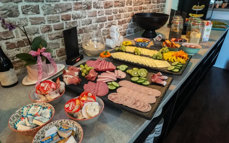 Frühstücksbuffet mit Käse- und Wurstplatten, Frischkäse und Obst vor Backsteinwand