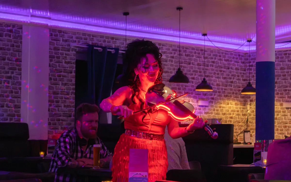 Live-Geigerin bei einem Abendevent im Küstenklub, Gäste an Tischen unter violettem Licht